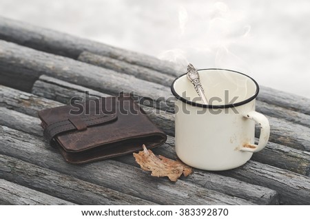 Vintage purse and old mug with a hot drink on a park bench with natural background in the outdoors. Photo in vintage color image style. Morning Still life.  Coffee break outdoors.