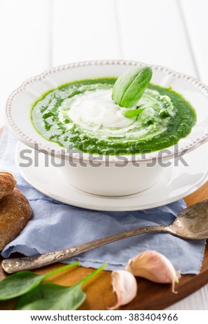 Traditional spinach cream soup with fresh spinach leaf on top on white wooden background, selective focus