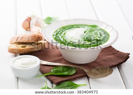 Traditional spinach cream soup with fresh spinach leaf on top on white wooden background, selective focus