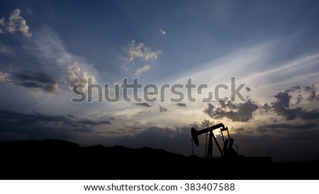 Silhouette of crude oil pump in oil field on a cloudy sunset.