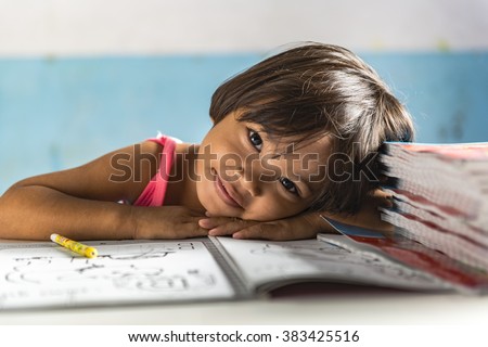 a very young girl student in the school has her head on the exercise book and smiling friendly. Thai school in a small village Royalty-Free Stock Photo #383425516