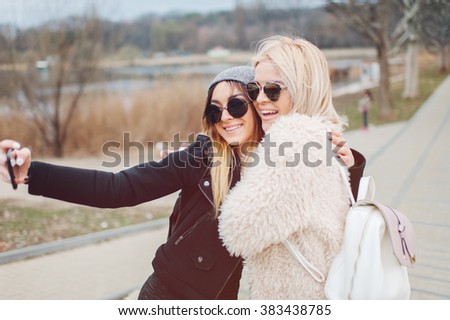 Outdoor lifestyle portrait of two best friends, smiling and having fun together, enjoy eachother company posing and makingselfie pictures to eachother and share happiness