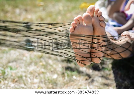 Closeup of happy family lying on hammock on sunny countryside background. Picture of man and children legs barefoot. 