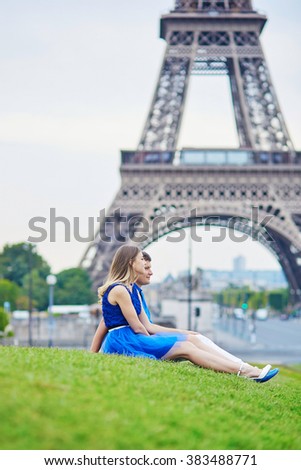 Romantic dating couple on Trocadero viewpoint in Paris, sitting on the grass and hugging tenderly, Eiffel tower is in the background
