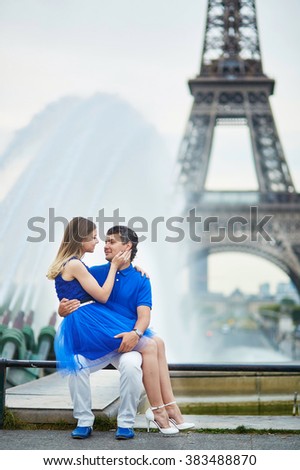 Romantic dating couple on Trocadero viewpoint in Paris, sitting near a fountain and hugging tenderly, Eiffel tower is in the background