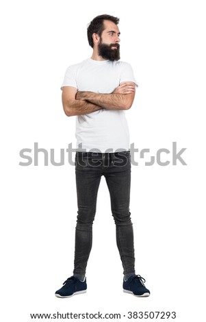 Serious bearded hipster in white t-shirt and tight jeans looking away. Full body length portrait isolated over white studio background.  Royalty-Free Stock Photo #383507293