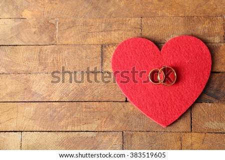 Red felt heart and wedding rings on wooden background closeup