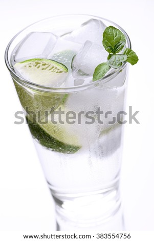 Single tall glass of cold ice water with mint leaves and lime slices over white background with reflection on table