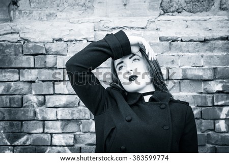 Portrait of a teenage girl with black lipstick posing next to an old brick wall. Black and white