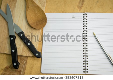 blank notebook and pen with kitchen utensils on wooden table.