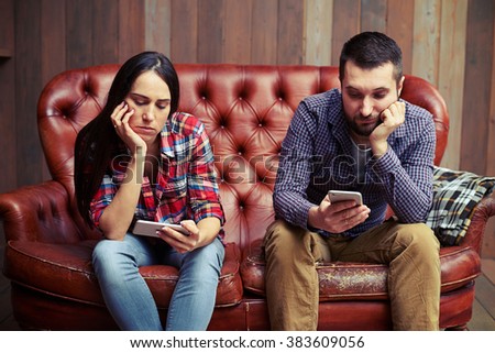 bored young couple sitting on couch and looking at their phones