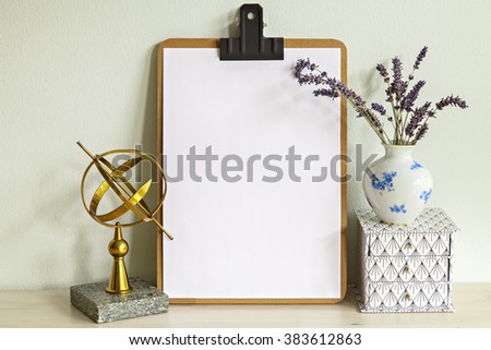 Image of clipboard mock up scene with vase, box and a brass sun dial. 