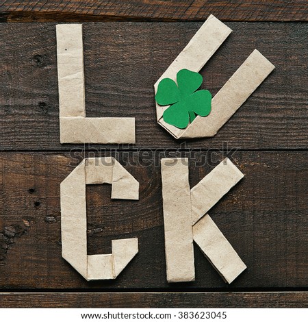 Craft paper origami LUCK lettering on dark barn wood rustic background. Green clover leaf. St. Patrick's Day greeting postcard template.