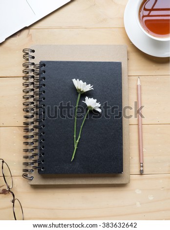 Closed notebook or diary with flower, laptop and cup of tea