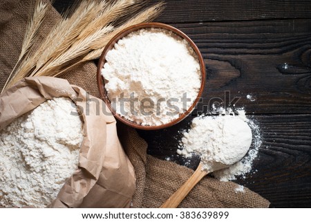 Flour in a wooden bowl, paper bag and spoon. Top view, space for text. Royalty-Free Stock Photo #383639899
