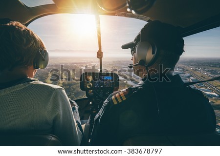 Inside view of a helicopter in flight, with man and woman pilots flying a helicopter on a sunny day. Royalty-Free Stock Photo #383678797
