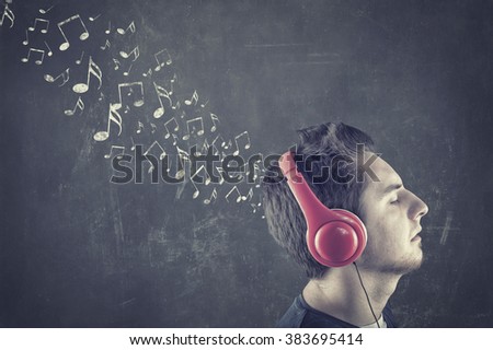 Teenager standing in front of a blackboard with musical notes drawn and listening to music on headphones