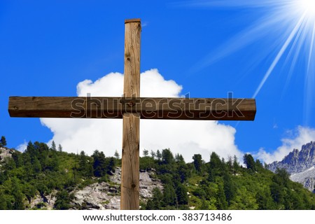 Wooden christian cross in mountain, Italian Alps, with blue sky, clouds and sun rays