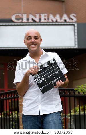 A young man or movie critic holding a movie directors clap board in front of the cinemas.