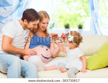 happy family in anticipation of the baby. Pregnant mother, father and child daughter paint colors on the tummy