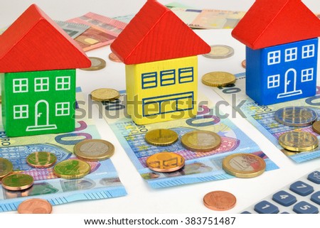 Three toy houses sitting on Euro notes and coins, with a calculator to symbolize home finance.