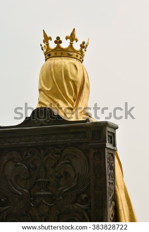 Head of king wearing gold crown and yellow veil while sitting on brown chair