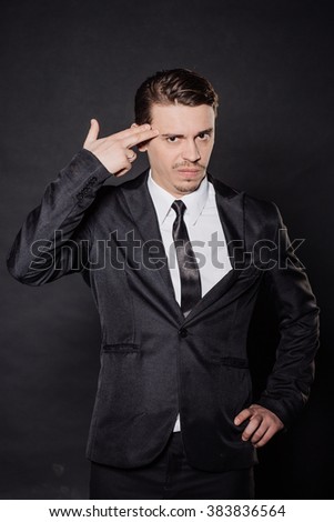 portrait young businessman in black suit gesturing with his finger against temple asking are you crazy? emotions, facial expressions, feelings, body language, signs. image on a black background.