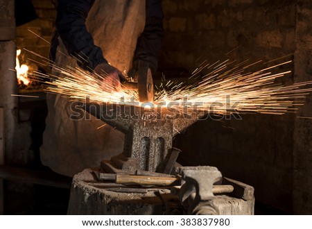 The blacksmith manually forging the molten metal on the anvil in smithy with spark fireworks Royalty-Free Stock Photo #383837980