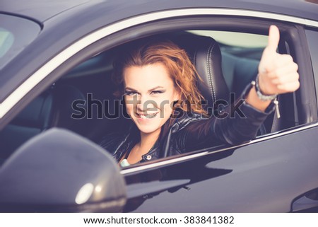 Young happy woman showing Ok sign, thumb up in a sport car 
