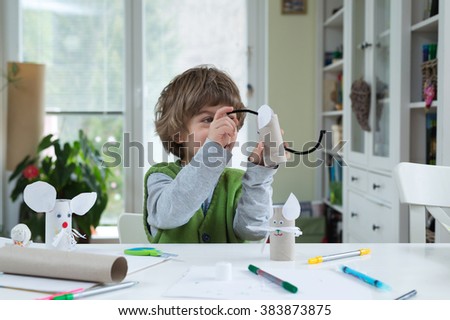 Little boy being creative making homemade do it yourself paper toys. Supporting creativity, learning by doing, learning through experience. Helping child gain access to a creative way of seeing. Royalty-Free Stock Photo #383873875