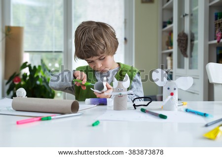 Little boy being creative making homemade do it yourself paper toys. Supporting creativity, learning by doing, learning through experience. Helping child gain access to a creative way of seeing. Royalty-Free Stock Photo #383873878
