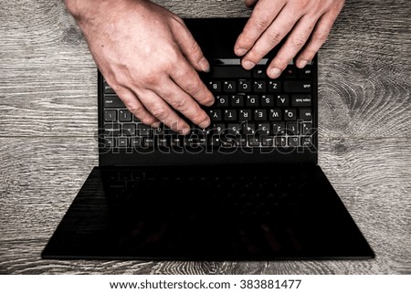 Black laptop on wood with hands viewed from above.
