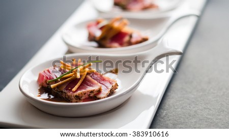 Tuna Tataki is a Japanese dish which consist of briefly seared tuna steak in thin slices. Served as appetizer with brandy sauce and garnish on a dark background. Royalty-Free Stock Photo #383910616