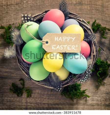 Easter eggs with feather decoration and tag on wooden background. Vintage style toned picture