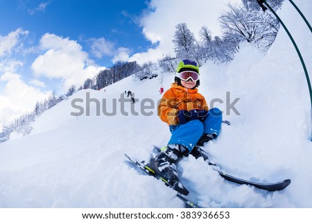 Child with ski  and wearing mask sit in snow