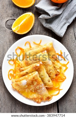 Delicious crepes with orange syrup on white plate over wooden background, top view Royalty-Free Stock Photo #383947714