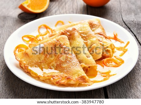Crepes Suzette on white plate over wooden background Royalty-Free Stock Photo #383947780