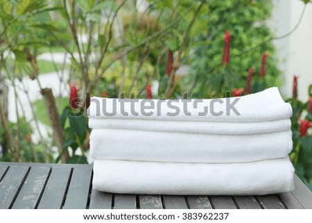 Stacked white spa cloth beach towels in garden background. 