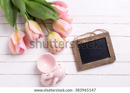 Spring  pink  tulips, decorative rabbit  and empty  blackboard on white  painted wooden background. Selective focus. Place for text. 