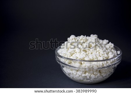 White fresh cheese in a glass bowl on a dark background. Contrast image, background, space for text.