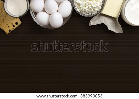 Dairy products such as cheese, yogurt, cottage cheese and eggs stacked on a brown background with stripes. Space for text