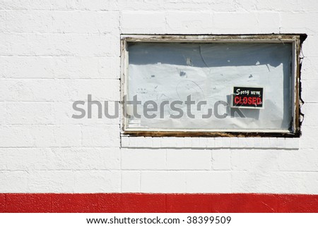 boarded up white window of bankrupt business with "Sorry we're closed" sign