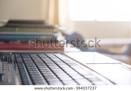 Close-up, soft focus keyboard with pile of books and bright natural light from window, selective focus, shallow depth of field