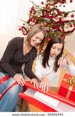 Two woman packing Christmas present in front of tree