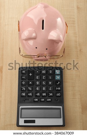 Pink piggy bank with glasses and calculator on light wooden background
