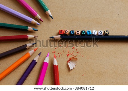 Colorful pencils arranged in half circular pattern with words Education on plastic alphabet block