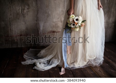 a bouquet of anemones in the hands of the bride against the background of textured walls Royalty-Free Stock Photo #384093940