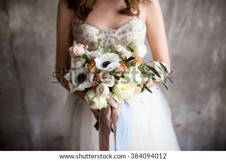 a bouquet of anemones in the hands of the bride against the background of textured walls Royalty-Free Stock Photo #384094012