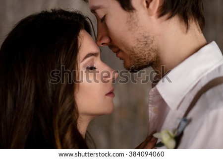 couple embrace on a background of textured walls in the loft, the bride in a wedding dress and beige with a bouquet of anemones in hand, groom in beige trousers and a white shirt with suspenders Royalty-Free Stock Photo #384094060