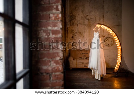 gentle wedding dress hanging on a semi-circular lamp glowing in the loft Royalty-Free Stock Photo #384094120